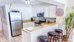Una cocina moderna con armarios blancos, un refrigerador de acero inoxidable, un microondas, una estufa y una isla grande con taburetes de bar.