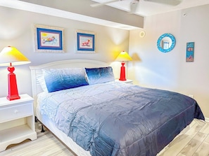 A bedroom with a bed, two bedside tables, two lamps, and wall decorations.