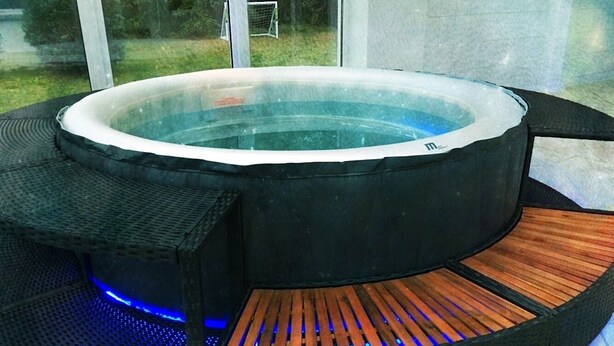 A hot tub with a wooden bench and a small seating area, surrounded by a black structure with a glass enclosure. - Ferienpark Canow (Wustrow)