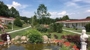 A garden with a pond, statues, and a row of white buildings with red roofs. - Ferienpark Canow (Wustrow)