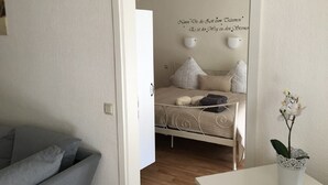 A bedroom with a bed, bedside lamps, a small table with a plant, and a grey sofa. - Ferienpark Canow (Wustrow)