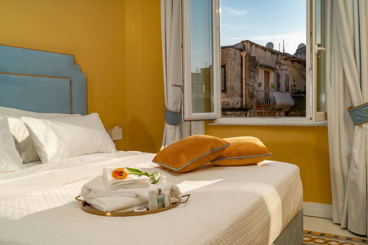 A hotel room with a bed, a window with curtains, and a tray with towels and toiletries.