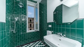 A bathroom with green tiles, a white sink, and a window with a view of an old building. - Il Fiore D'Oro Luxury (Naples)