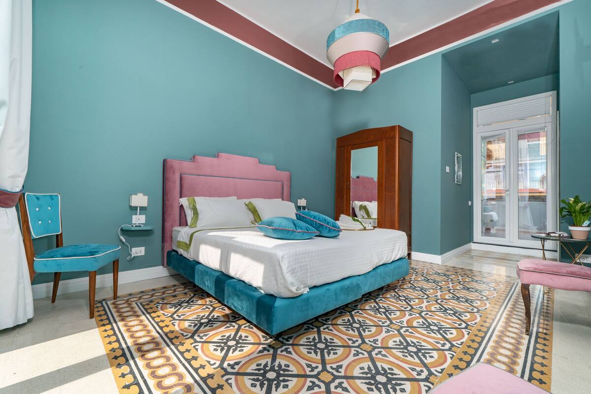 A bedroom with a bed, a chair, a nightstand, a mirror, and a window.