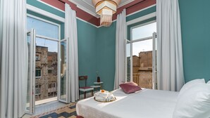 A hotel room with a bed, a small table, a chair, and a view of the city through large windows. - Il Fiore D'Oro Luxury (Naples)