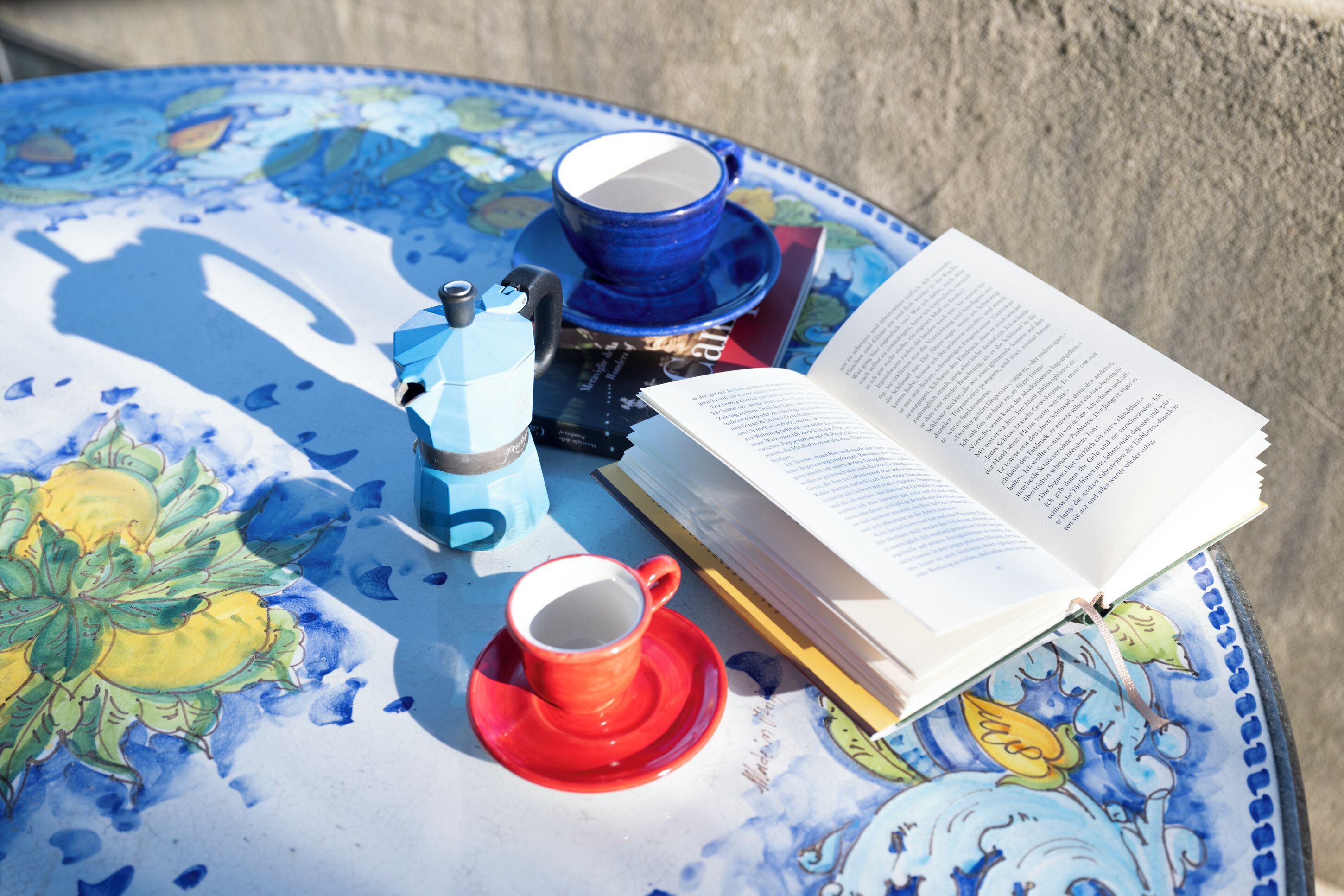 Une table sur laquelle se trouvent un livre, une tasse bleue et une tasse rouge, et dont le plateau est décoré d’un motif floral.