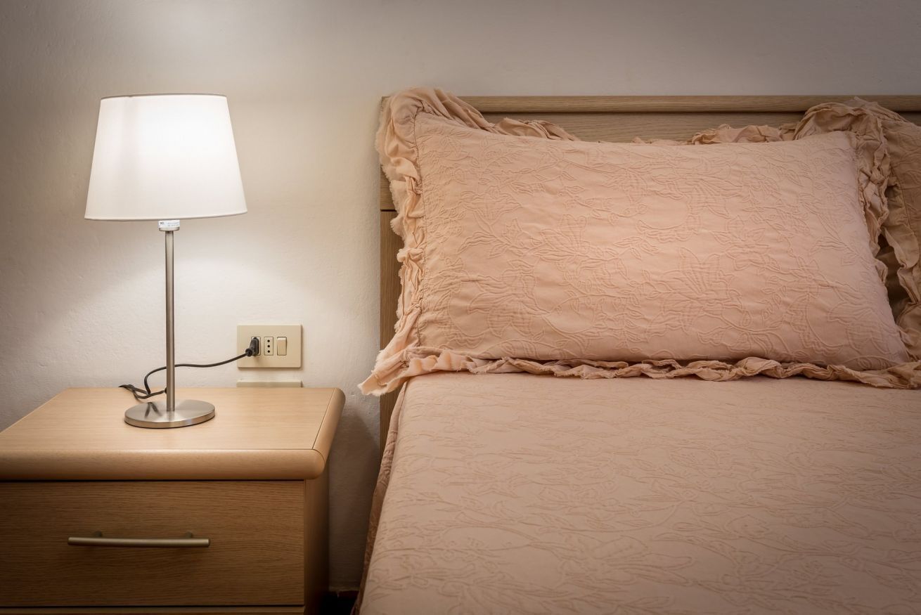 A bed with a ruffled pillow and a bedside table with a lamp.