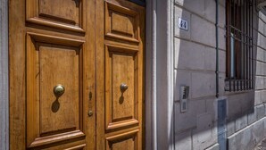 Eine hölzerne Doppeltür mit Messinggriffen, darüber die Hausnummer '44' und ein Fenster mit Metallgitter zur Rechten.