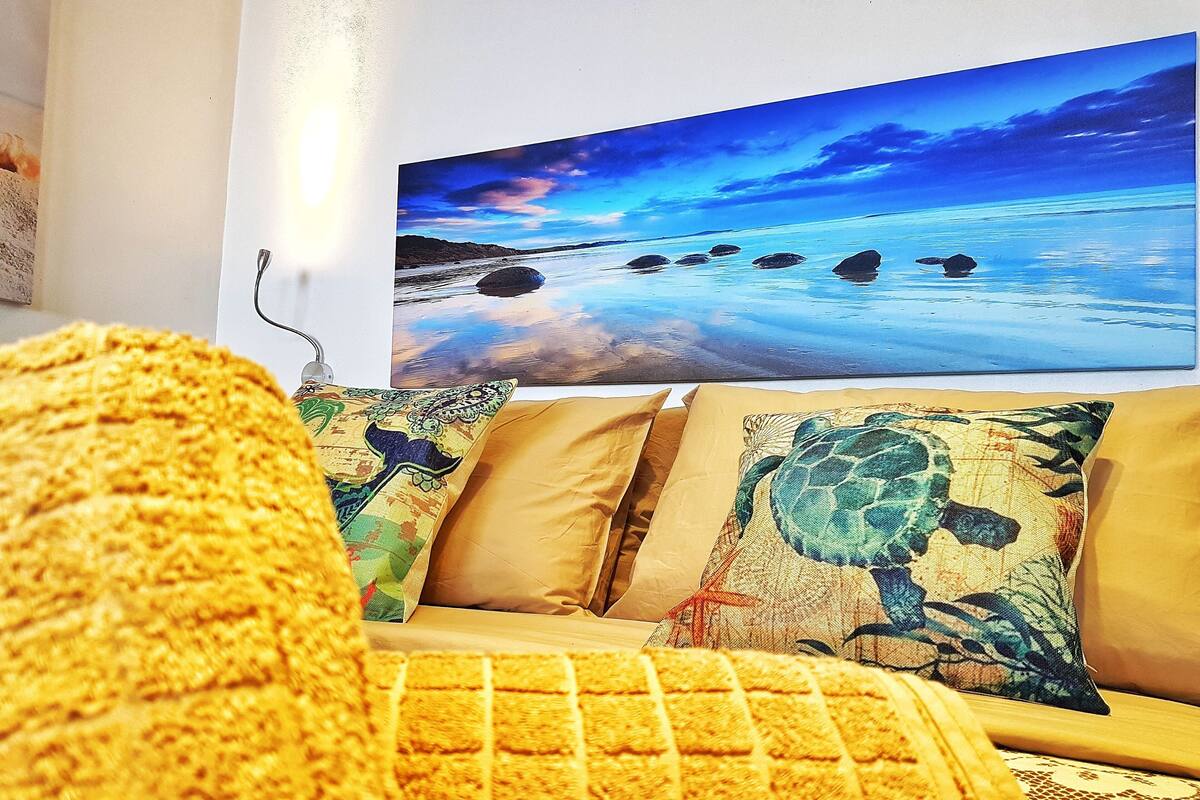 A living room with a sofa, a large painting of a beach scene, and a turtle pillow.