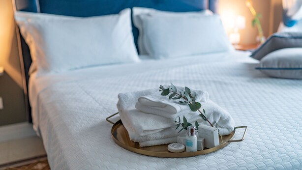 Una cama bien hecha con ropa blanca, una bandeja con toallas dobladas y artículos de aseo.