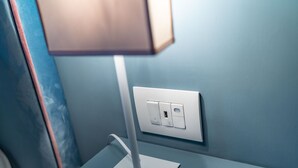 Una habitación moderna con una mesita de noche blanca, una lámpara y un enchufe en la pared.