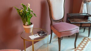 Una habitación con una silla, una mesita con una planta y una revista, y una alfombra estampada.