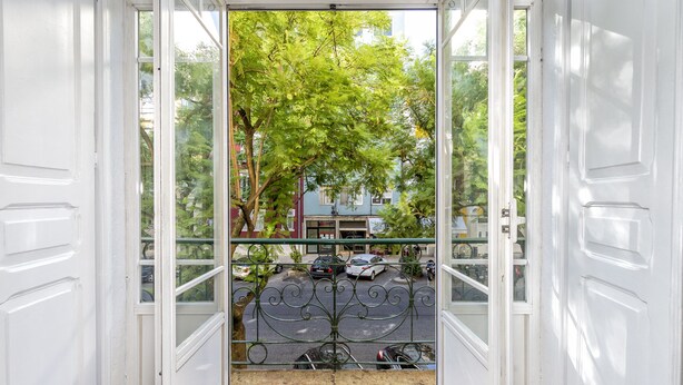 A view through a white door with a metal gate, leading to a street with parked cars and a building in the background. - 5 Bedroom Family  Apartment (Lisboa)