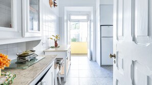 A narrow kitchen with white cabinets, a countertop, and a door leading to a balcony. - 5 Bedroom Family  Apartment (Lisboa)