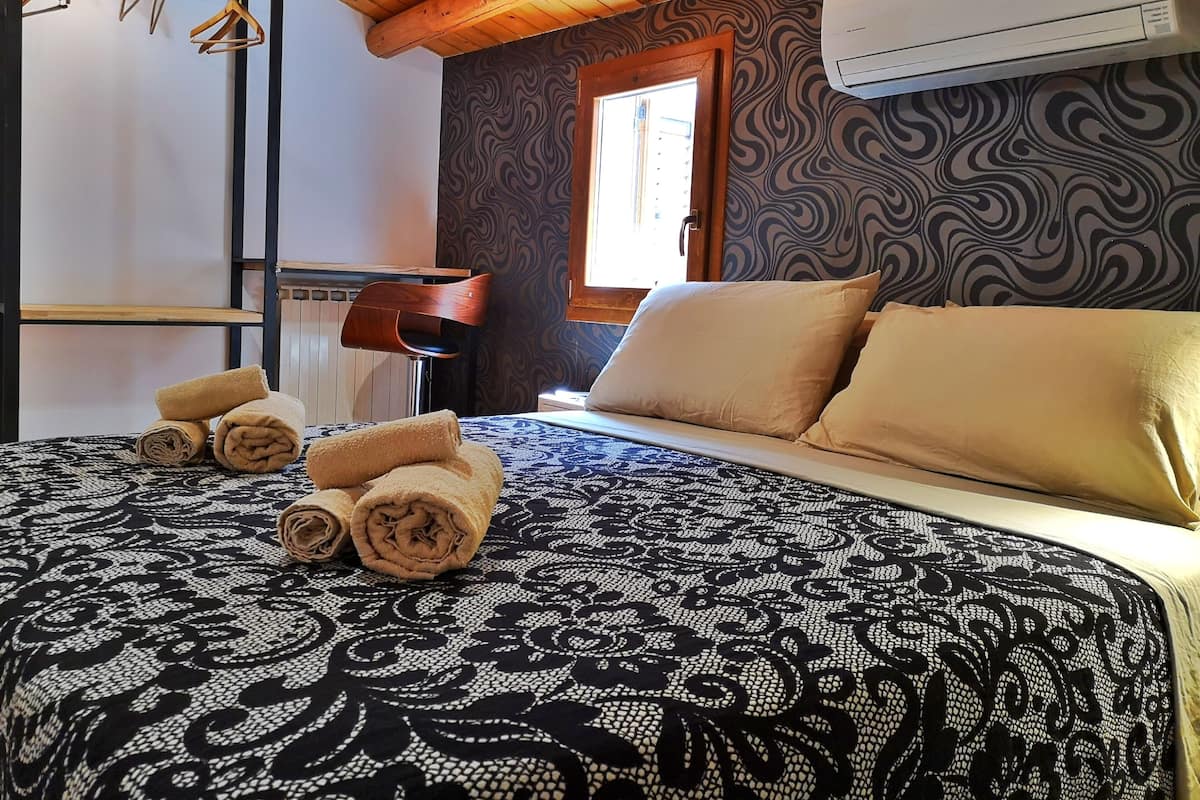 Une chambre d’hôtel avec un lit, des serviettes roulées, un plafond en bois, un appareil de climatisation et un mur à motifs.