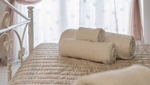 A neatly made bed with rolled towels, a metal bed frame, and sheer curtains with a subtle pattern. - Il Tulipano Verde B&B (Putignano)