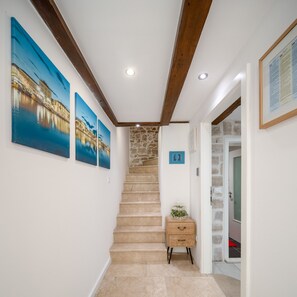 A staircase leading to a landing with a stone wall, a wooden cabinet, and three framed pictures on the wall.