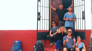 A group of people sitting on steps in front of a building with a red and white facade, a black metal gate, and a sign above the gate. - the heart of cusco  (Cusco)