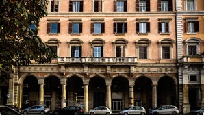 Um edifício de vários andares com estilo arquitetônico clássico, com janelas em arco e uma entrada central com varanda.