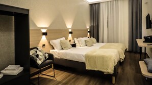Quarto de hotel moderno com uma cama grande, duas mesas de cabeceira, uma escrivaninha e um espaço para sentar.