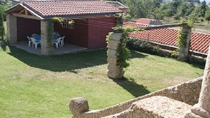 Ein kleines rotes Gebäude mit einem Ziegeldach, einer Terrasse mit weißen Stühlen und einer Steinmauer.