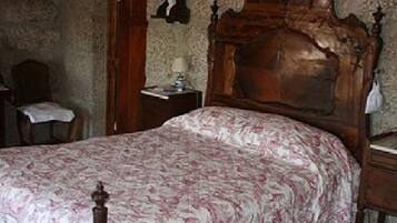 A bedroom with a wooden bed frame, a bedside table with a lamp, and a chair with a table.