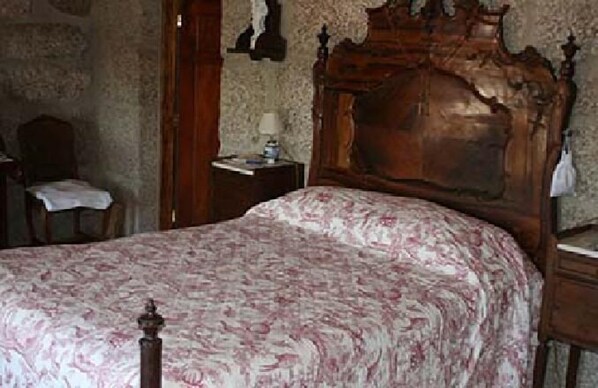 Un dormitorio con estructura de cama de madera, una mesita de noche con lámpara y una silla con una mesa.