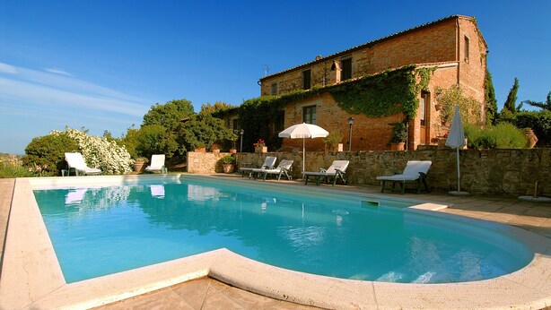 A swimming pool with lounge chairs and an umbrella, surrounded by a stone wall and vegetation. - Tenuta S. Agnese (Montepulciano)