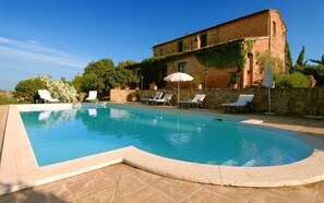 A swimming pool with lounge chairs and an umbrella, surrounded by a stone wall and vegetation. - Tenuta S. Agnese (Montepulciano)