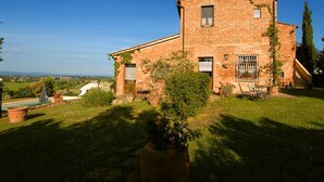 A brick building with a garden, a small pond, and a clear view of the countryside. - Tenuta S. Agnese (Montepulciano)