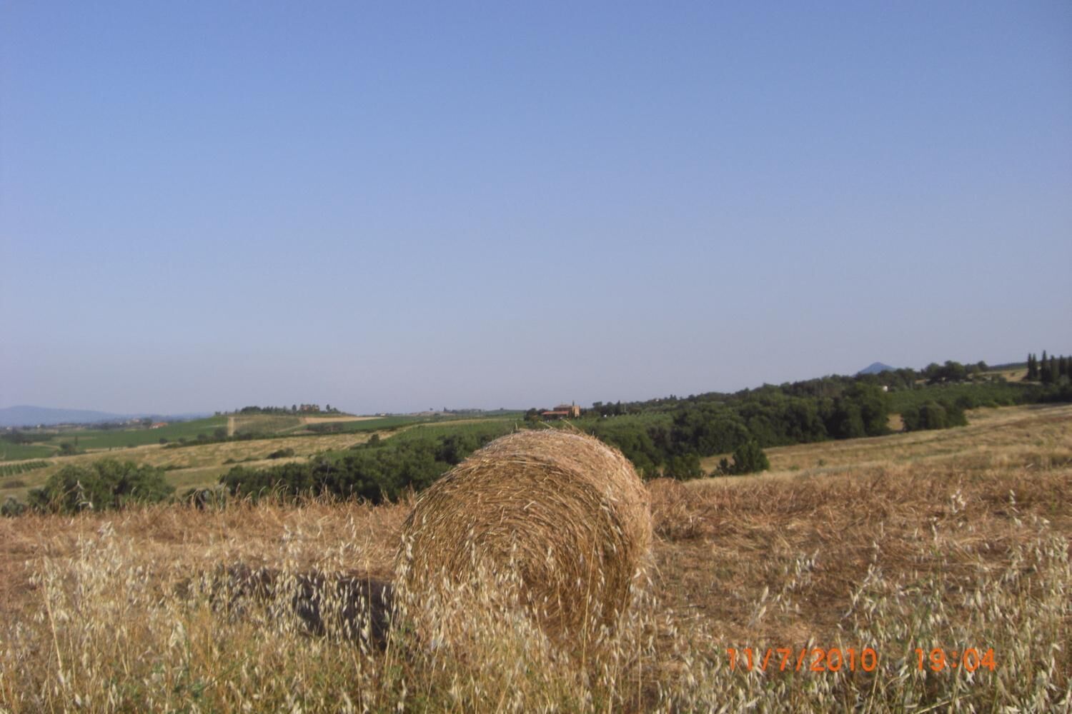 A rural landscape with a hay bale in the foreground and a clear blue sky.