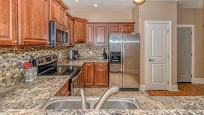 A kitchen with wooden cabinets, a stainless steel refrigerator, a microwave, an oven, and a sink.
