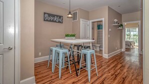 A kitchen with a white table, blue bar stools, a hanging light fixture, and a 'thankful' sign on the wall.