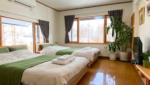 A hotel room with two beds, large windows, a flat-screen TV, and several potted plants. - Ritz Garden Niji (Biei)