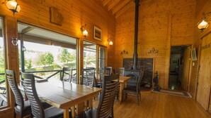 A wooden interior with a dining area, a fireplace, and a view through large windows. - Ritz Garden Niji (Biei)