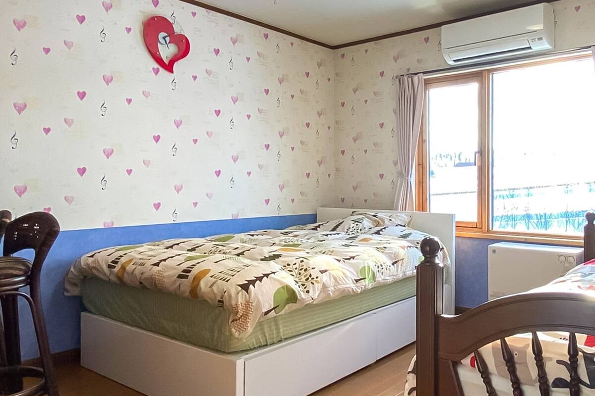 Un dormitori amb un llit, una cadira, un aparell d'aire condicionat i una finestra amb cortines.