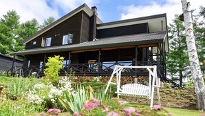 A two-story house with a covered porch, surrounded by a garden with various plants and flowers. - Ritz Garden Niji (Biei)