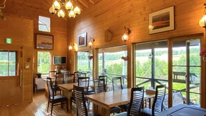 A wooden interior with tables and chairs, large windows, and a mounted deer head. - Ritz Garden Niji (Biei)