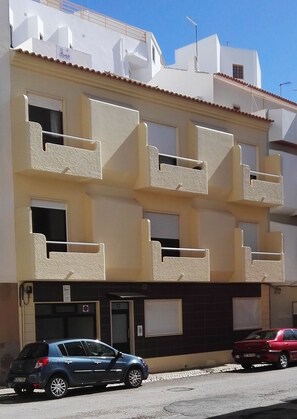 A multi-story building with balconies, a garage, and parked cars.
