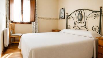 A bedroom with a bed, a chair, a wooden nightstand, a radiator, and a window with curtains.