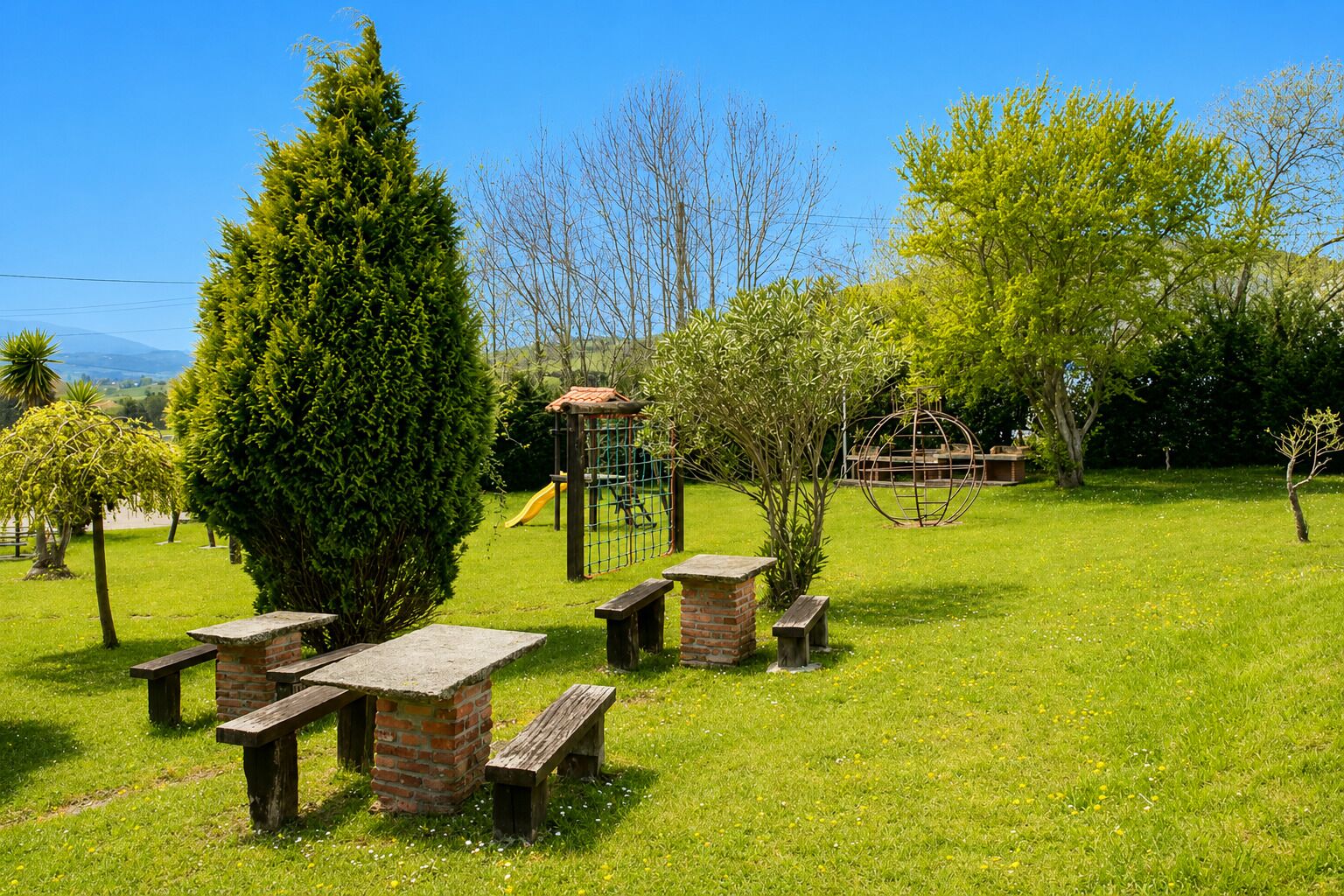 A grassy outdoor area with picnic tables, a playground, and a spherical sculpture.