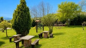 A grassy outdoor area with picnic tables, a playground, and a spherical sculpture.