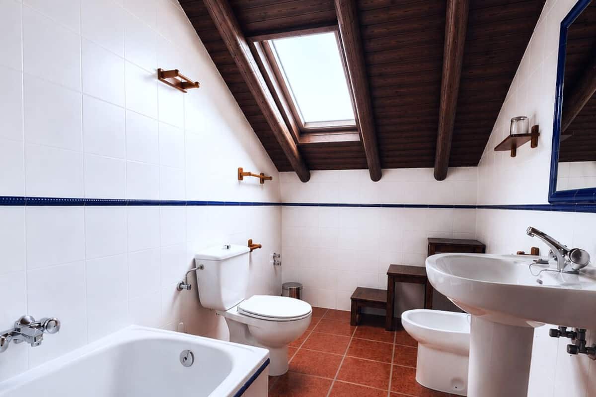 A bathroom with a bathtub, toilet, and sink, wooden beams on the ceiling, and a skylight.