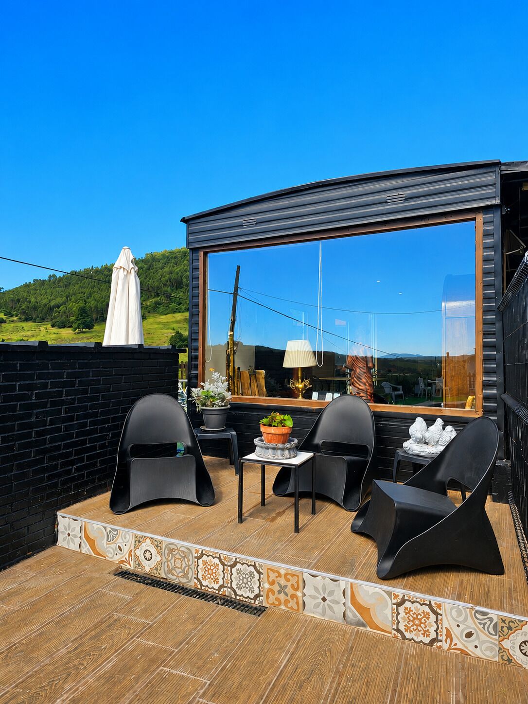 Un espacio moderno para sentarse al aire libre, con un ventanal grande, una mesa, sillas y una planta en maceta.