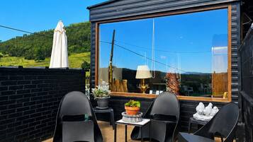 Un espacio moderno para sentarse al aire libre, con un ventanal grande, una mesa, sillas y una planta en maceta.