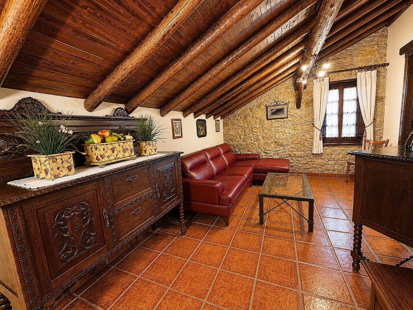 Un interior rústico con techo de madera, pared de piedra, sofá de cuero y un aparador de madera con adornos.