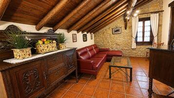Un interior rústico con techo de madera, pared de piedra, sofá de cuero y un aparador de madera con adornos.