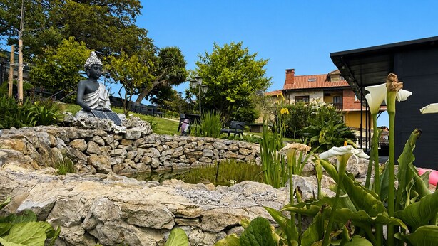 Un jardin agrémenté d’une statue, d’un mur en pierre et de différentes plantes.
