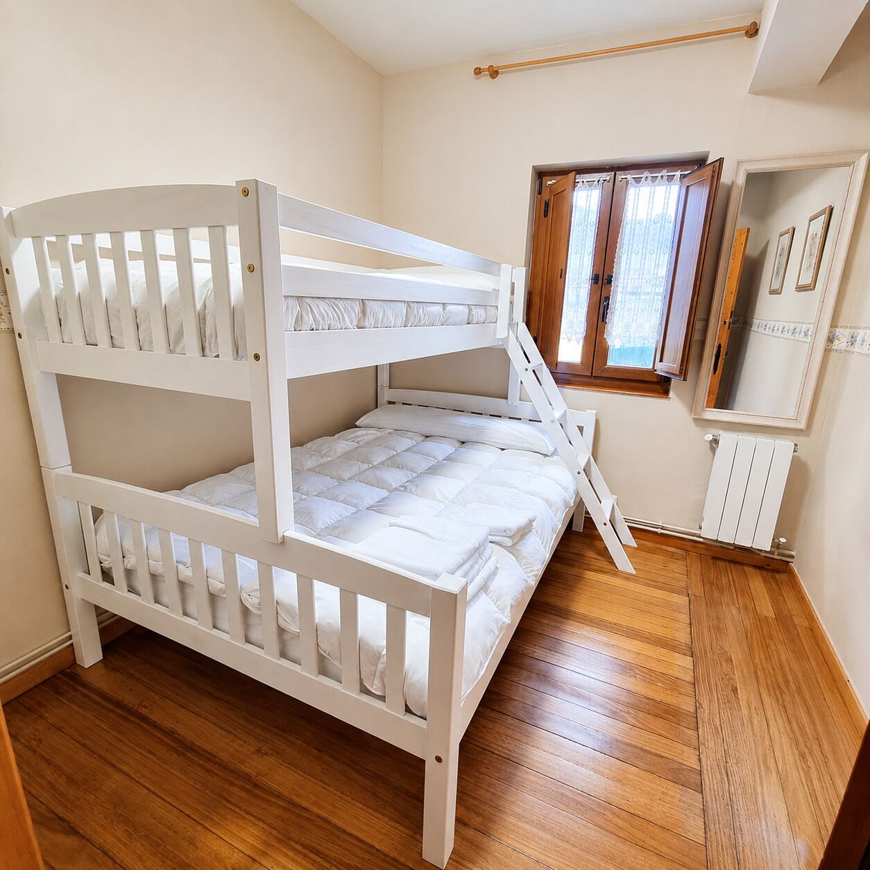 Ein Stockbett in einem Zimmer mit Holzboden, einem mit Vorhängen versehenen Fenster und einer Heizung.