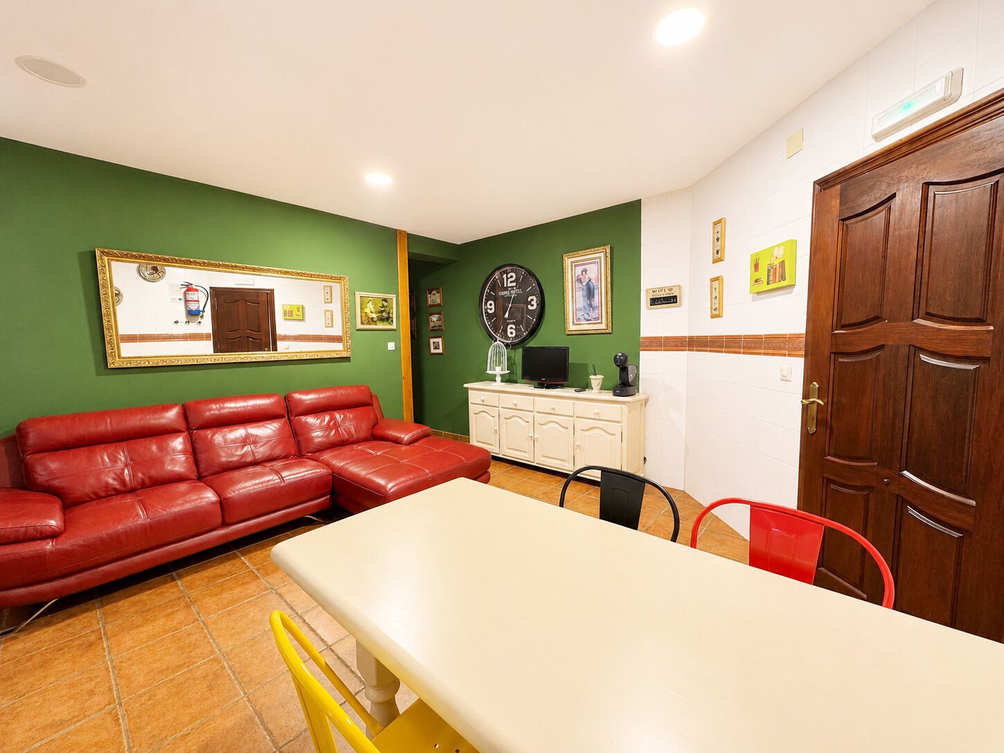 Ein Zimmer mit einem roten Ledersofa, einem weißen Tisch, einer Uhr, einem Schrank und einer Tür.